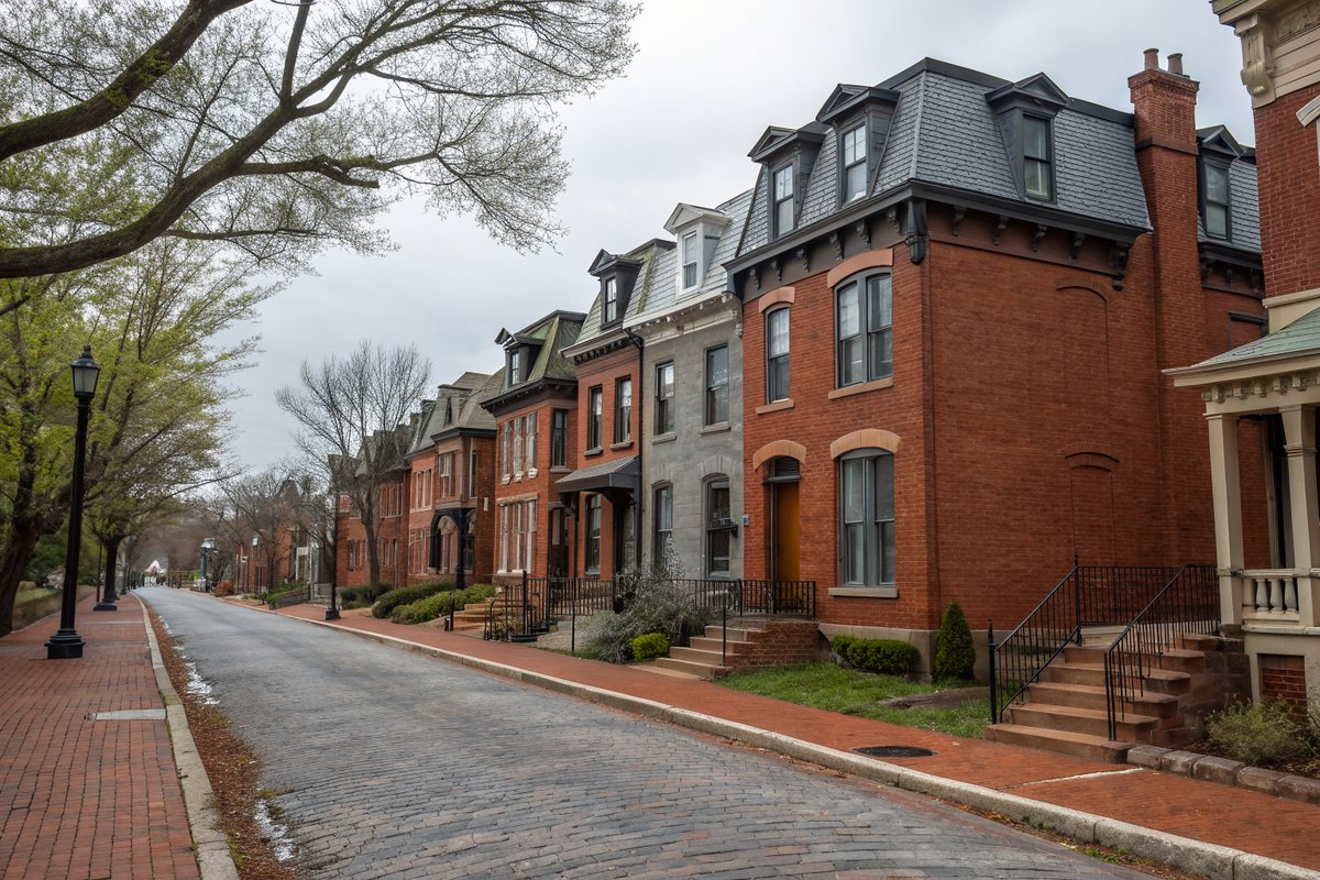 A row of restored brick townhouses with tall windows along an older brick-paved street